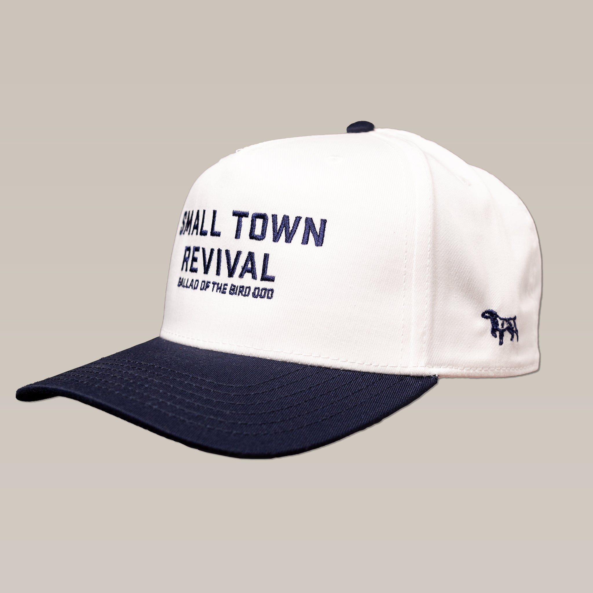 The Shop Hat by Ballad of the Bird Dog is a white and navy baseball cap with "Small Town Revival Ballad of the Bird Dog" embroidered on the front and a small dog logo on the side.