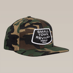 The Shop Hat by Ballad of the Bird Dog features a camo snapback and a "SMALL TOWN REVIVAL, BRENHAM TEXAS" patch—ideal for fans of small town style and Brenham-inspired hats.