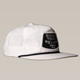 The Ballad of the Bird Dog Shop Hat features a black "Small Town Revival Brenham Texas" patch on a white snapback, perfect for small town patch hat fans. Shown on a plain beige background.