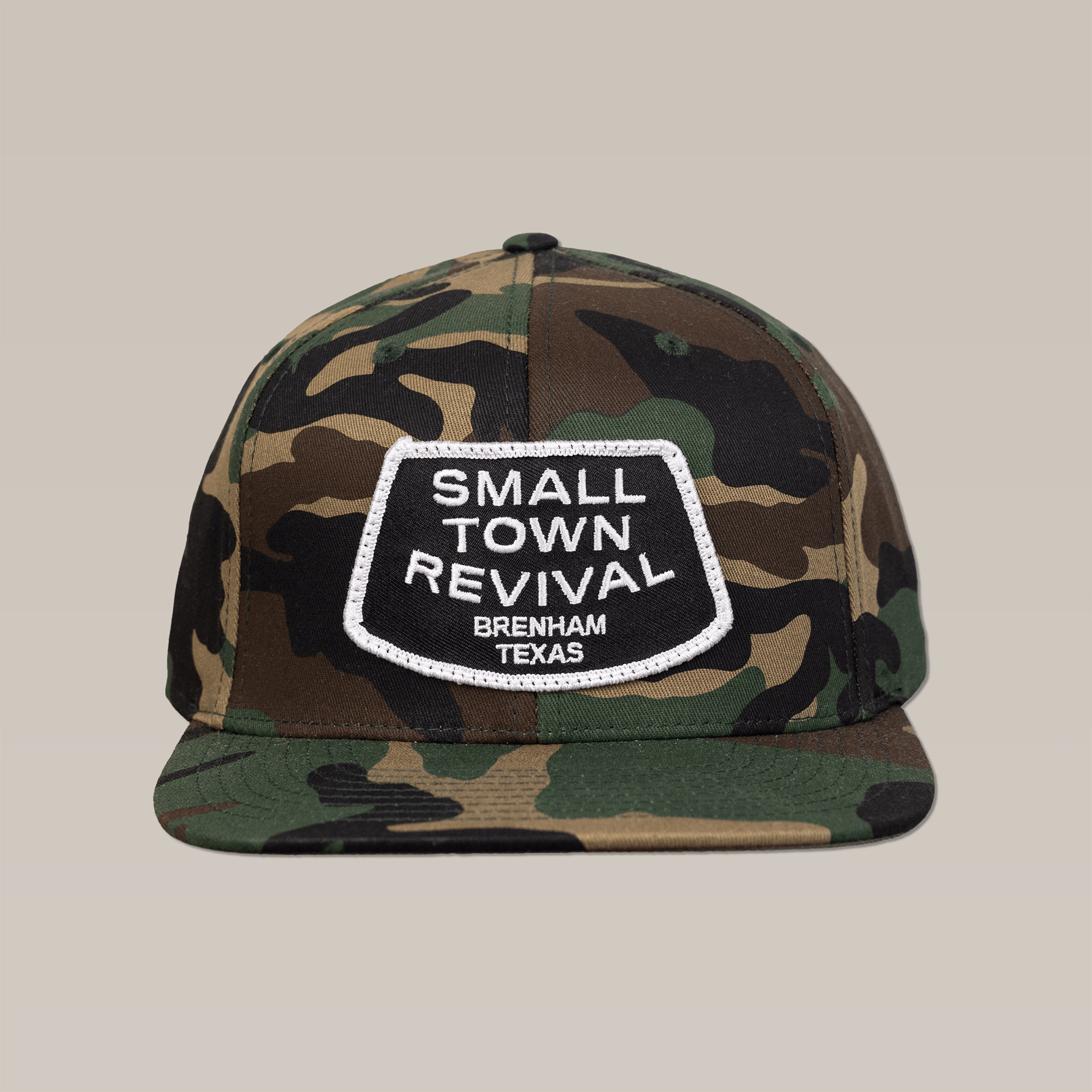 The Shop Hat by Ballad of the Bird Dog features a camouflage design with a white "SMALL TOWN REVIVAL BRENHAM TEXAS" patch—perfect for fans of small town pride and unique patch hats.