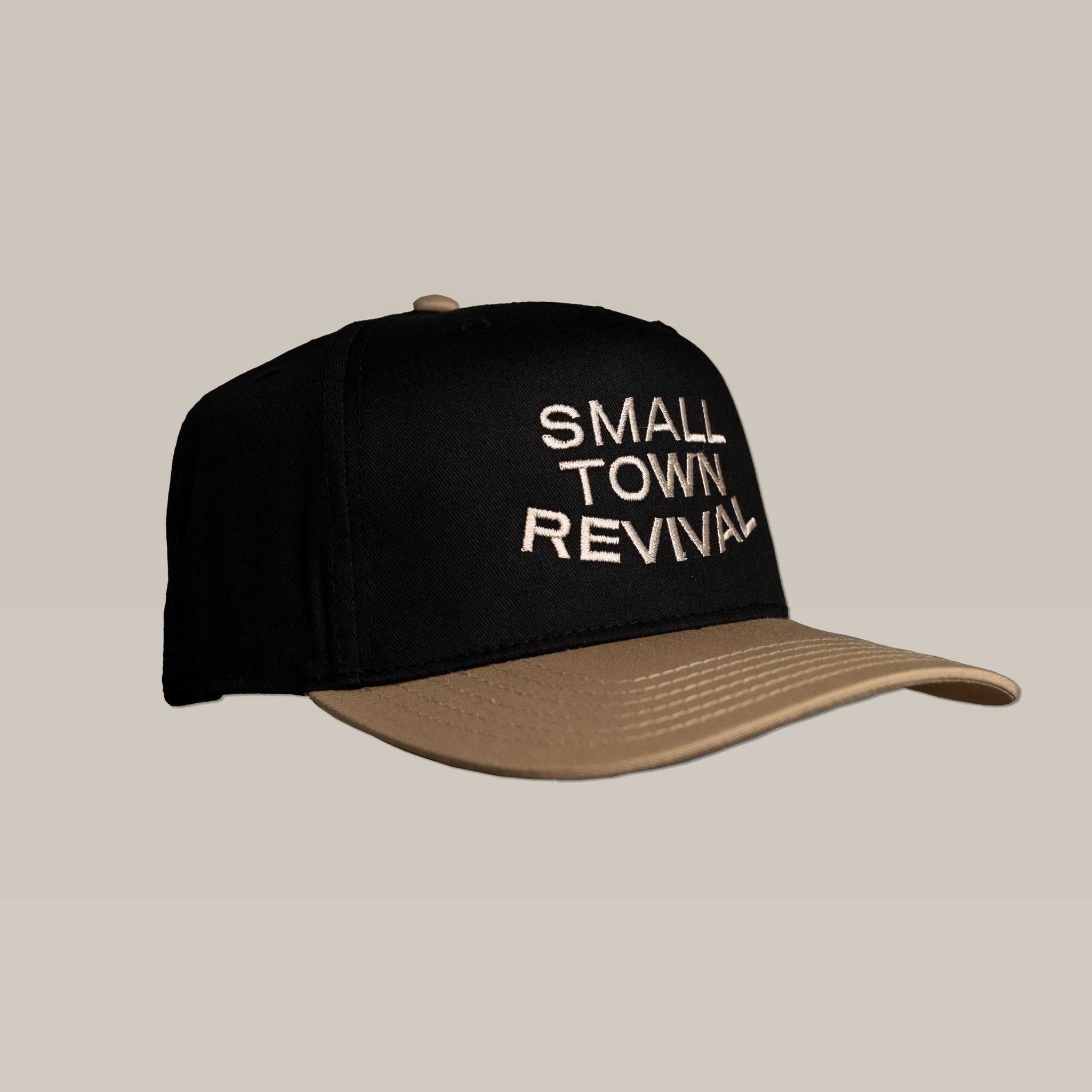 The Shop Hat | Small Town Revival Stitch by Ballad of the Bird Dog is a black and tan unstructured cap with "SMALL TOWN REVIVAL" embroidered in white on the front, adjustable snapback, shown against a plain beige background.