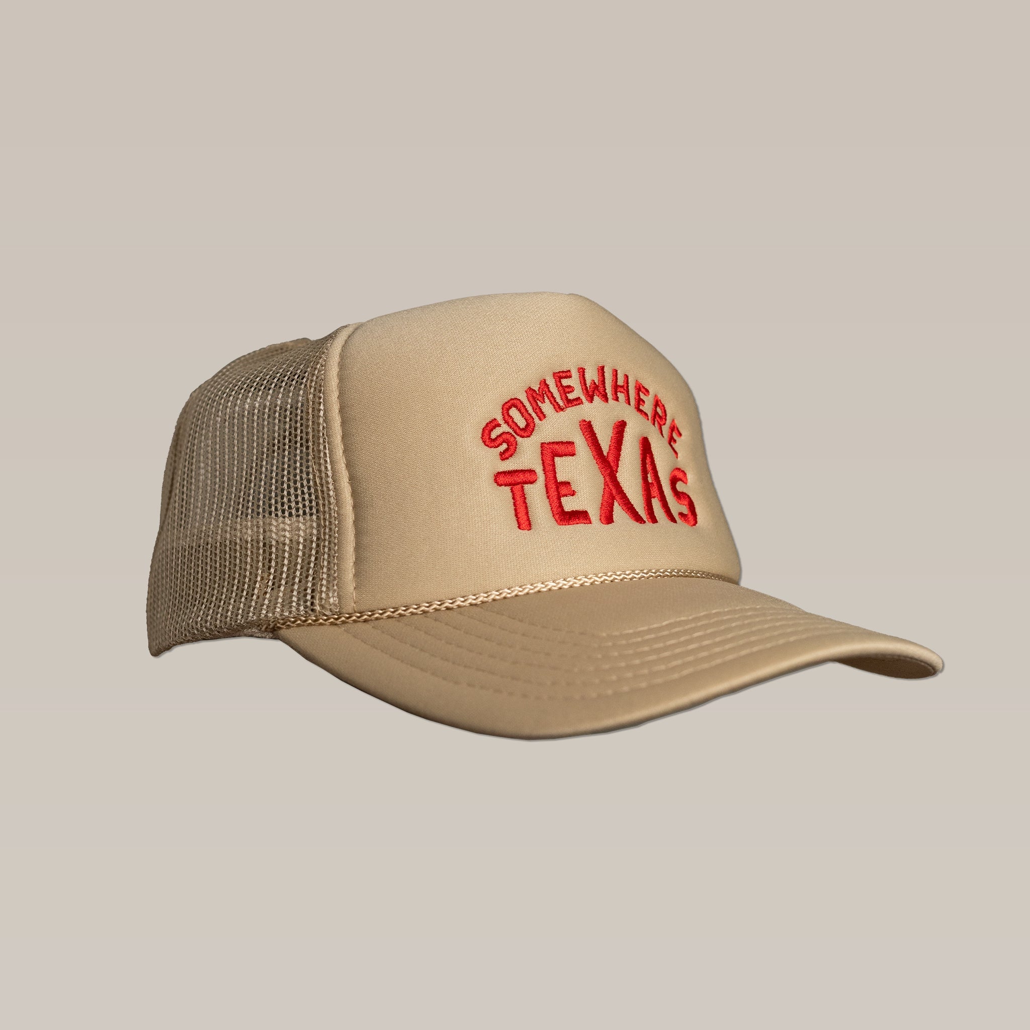 The Shop Hat by Ballad of the Bird Dog is a beige mesh snapback trucker hat with red "Somewhere Texas" embroidery on the front, designed in collaboration with Carra Sykes.