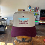 The Shop Hat | Thunderbird by Ballad of the Bird Dog, featuring beige and maroon colors, blue boat embroidery, and "TRUST YOUR GUT BRENHAM, TX" text, is displayed indoors on a metal stand.