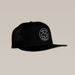 The Ballad of the Bird Dog Shop Hat is a black mesh SnapBack trucker cap with a circular "Trust Your Gut, Ballad of the Bird Dog" stitched logo patch on the front, displayed against a plain beige background.