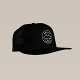 The Ballad of the Bird Dog Shop Hat is a black mesh SnapBack trucker cap with a circular "Trust Your Gut, Ballad of the Bird Dog" stitched logo patch on the front, displayed against a plain beige background.