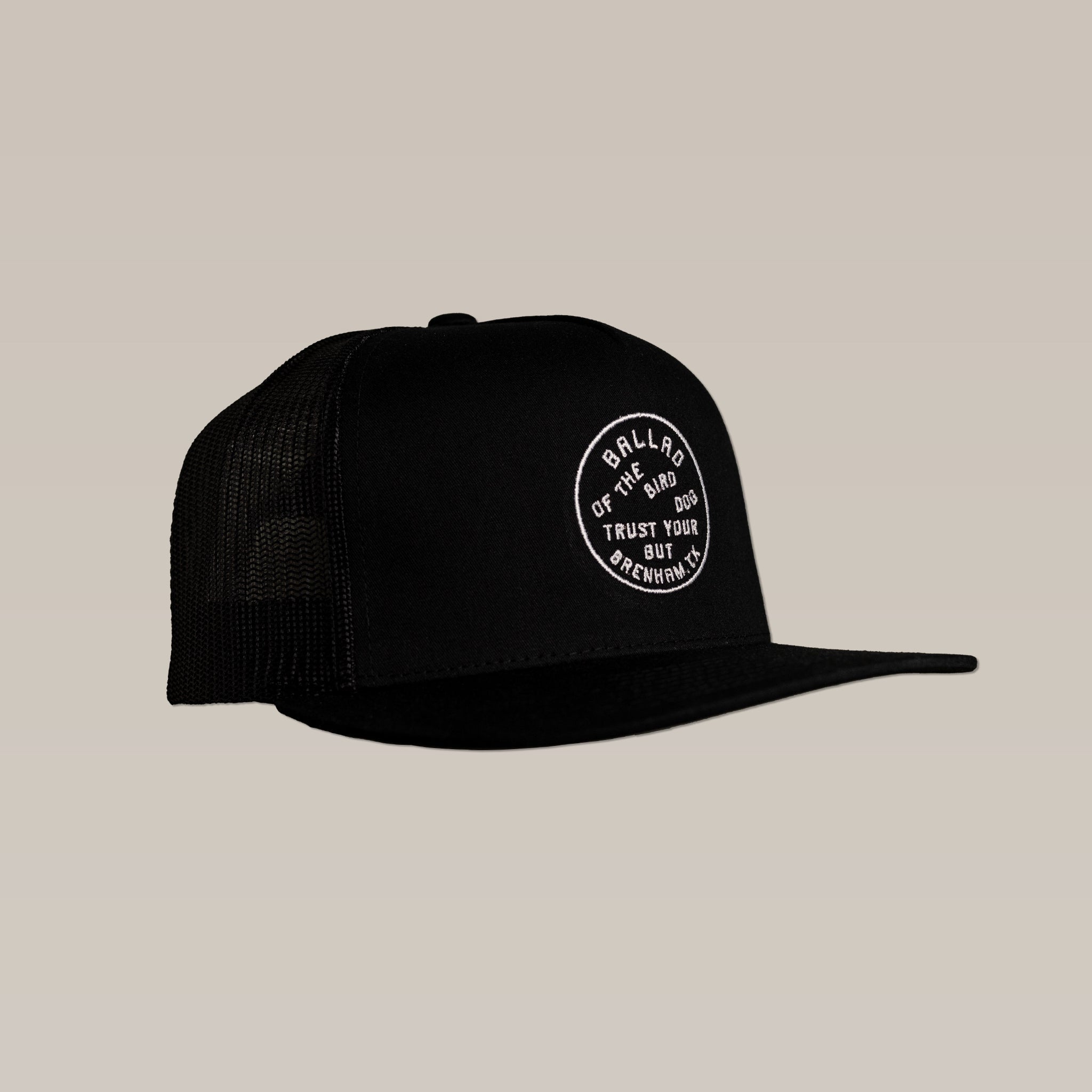 The Ballad of the Bird Dog Shop Hat is a black mesh SnapBack trucker cap with a circular "Trust Your Gut, Ballad of the Bird Dog" stitched logo patch on the front, displayed against a plain beige background.