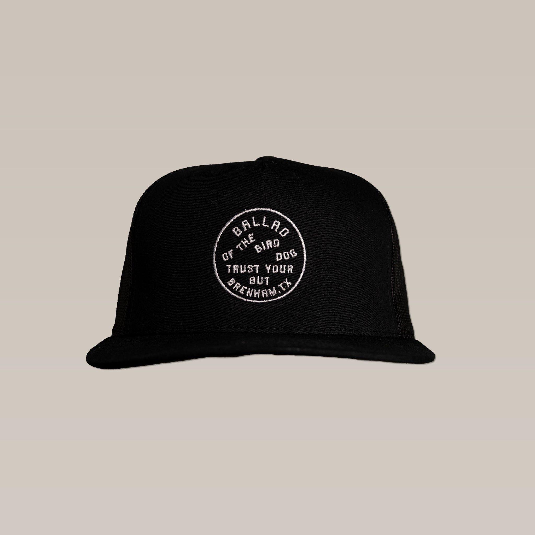 The Ballad of the Bird Dog Shop Hat | Trust Your Gut is a black mesh SnapBack cap featuring a stitched circular patch with "BALLARD THE BIRD DOG TRUST YOUR GUT OPENHAM TX" on the front, shown against a plain beige background.
