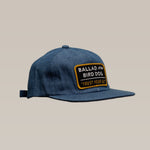 The Ballad of the Bird Dog Shop Hat | Trust Your Gut Vintage Slate features blue denim, a bold “TRUST YOUR GUT” patch in black, white, and yellow, and stands out against a plain beige background.