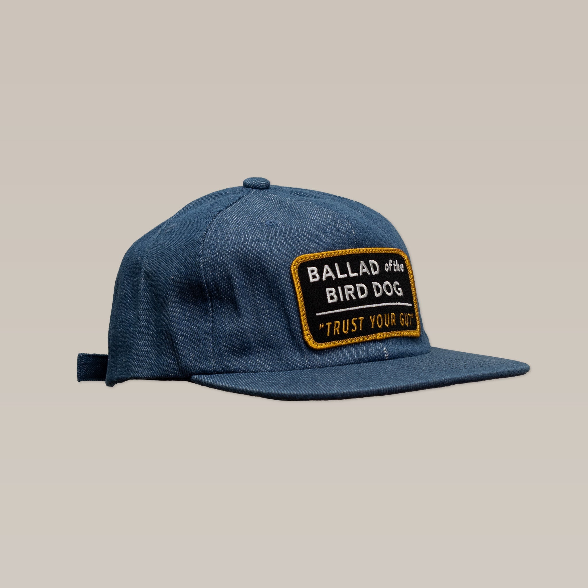 The Ballad of the Bird Dog "Trust Your Gut" Vintage Slate Shop Hat features blue denim and a front rectangular patch with "BALLAD of the BIRD DOG" and "TRUST YOUR GUT.