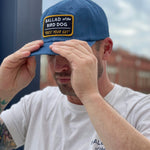 A man in the Ballad of the Bird Dog Shop Hat | Trust Your Gut Vintage Slate adjusts his snapback brim outdoors with buildings in the background, pairing it with a matching T-shirt.