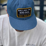 Person in a Ballad of the Bird Dog Shop Hat—Trust Your Gut Vintage Slate—and a matching white tee, both featuring the brand's logo.