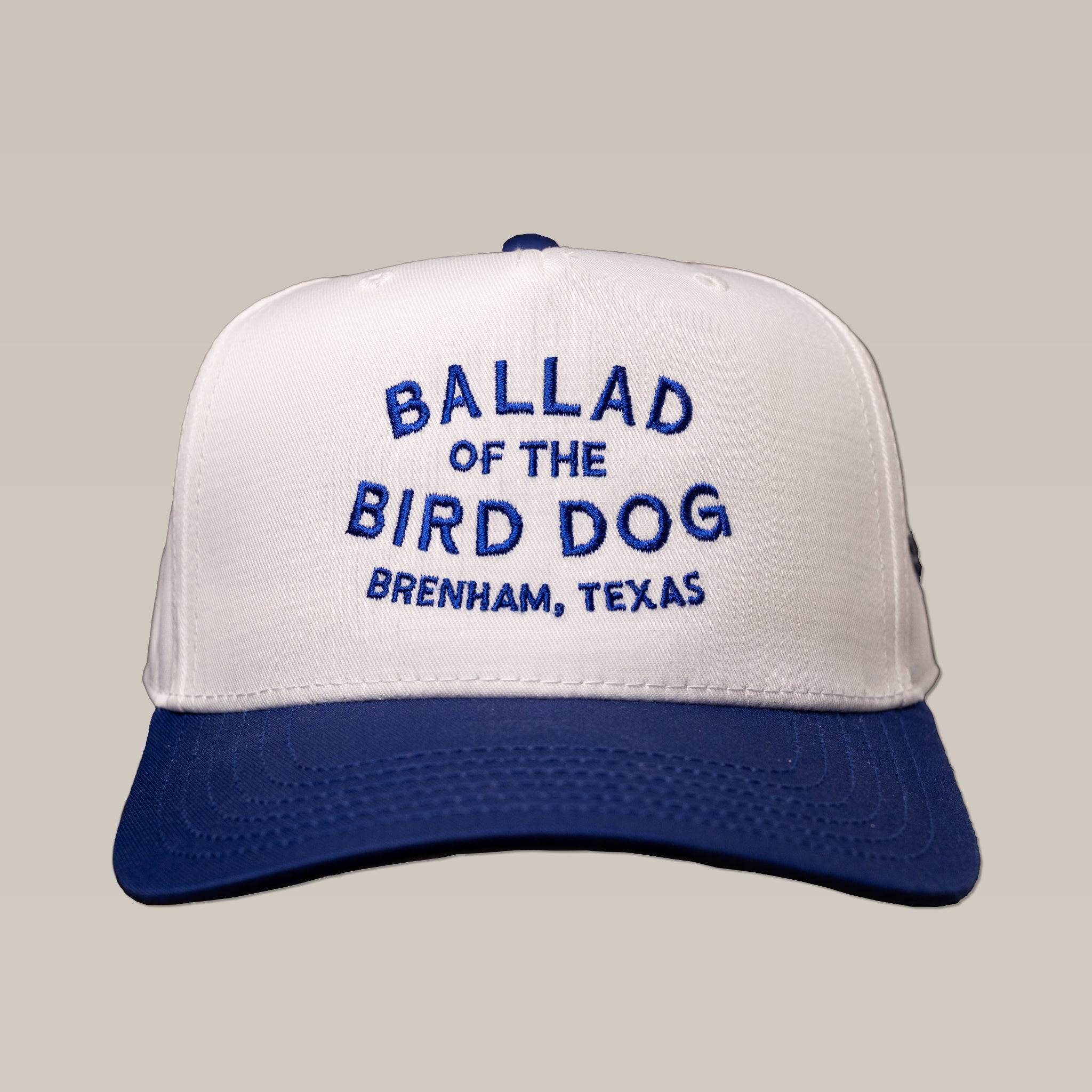 The Shop Hat | Updated Oval by Ballad of the Bird Dog is a white and blue trucker hat with "BALLAD OF THE BIRD DOG BRENHAM, TEXAS" embroidered in blue on the front.