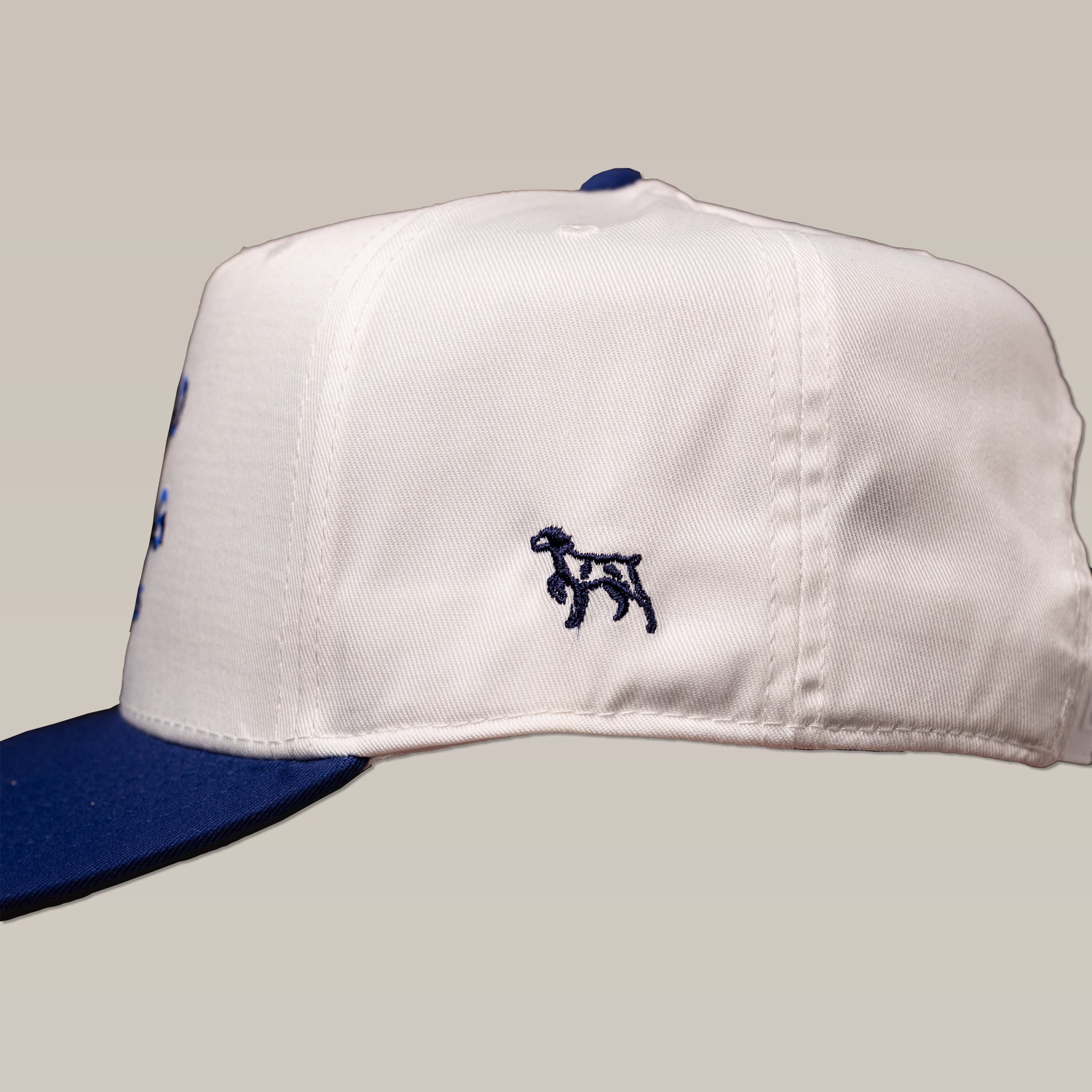The Shop Hat | Updated Oval by Ballad of the Bird Dog is a white baseball cap with a dark blue brim and a small embroidered dog logo on the side.