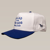 The Ballad of the Bird Dog Shop Hat features an updated oval design, white and blue colors, "Ballad of the Bird Dog, Brenham, Texas" embroidered on the front, and a small dog logo on the side.