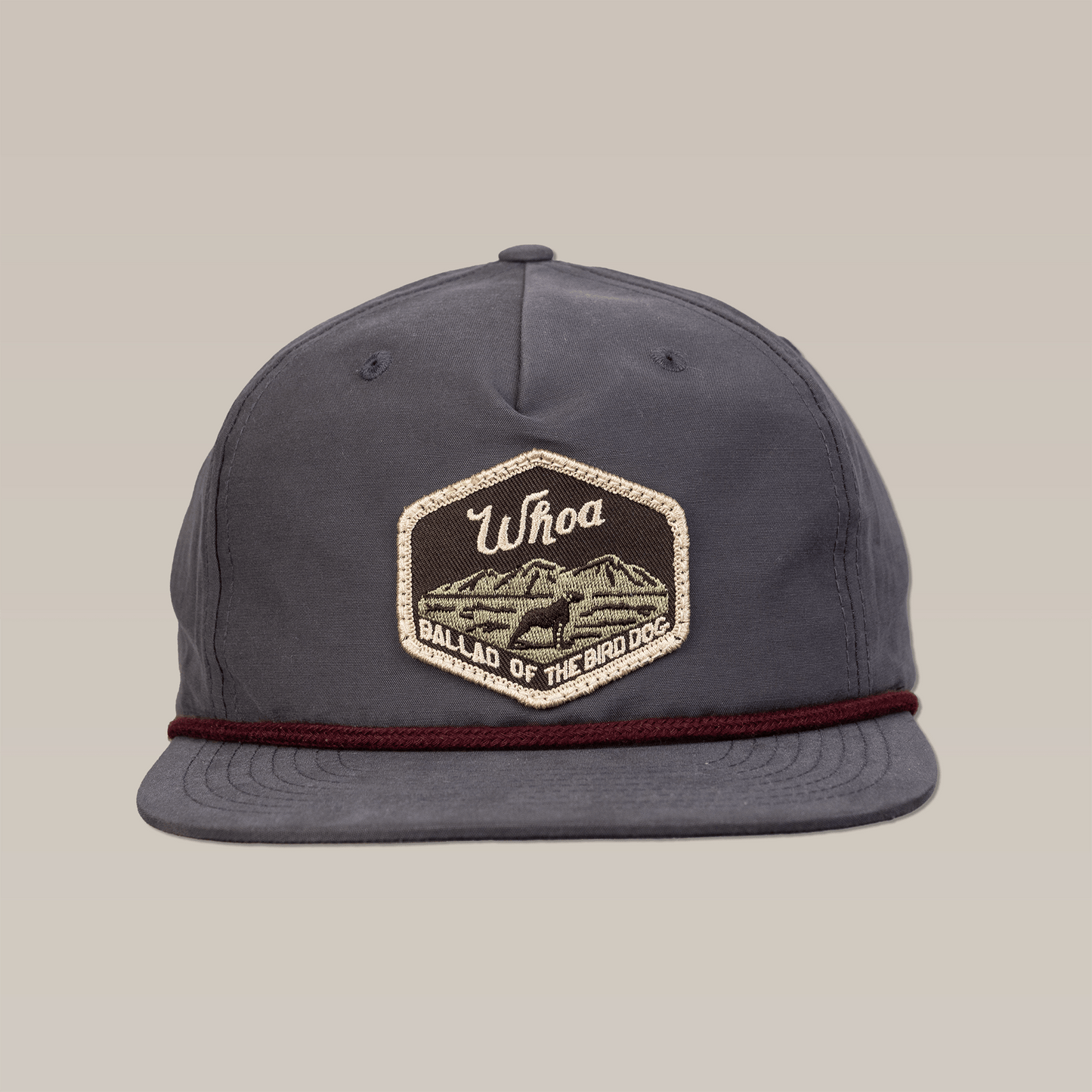 The Shop Hat | Whoa by Ballad of the Bird Dog features a gray patch with mountains and "Whoa" text, plus a burgundy cord above the brim—ideal for bird dog lovers.