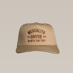 The Shop Hat | Worth The Trip by Mescalito Coffee is a beige travel hat with brown "Mescalito Tex Coffee USA Worth The Trip" embroidery—ideal for coffee lovers seeking laid-back adventure style.