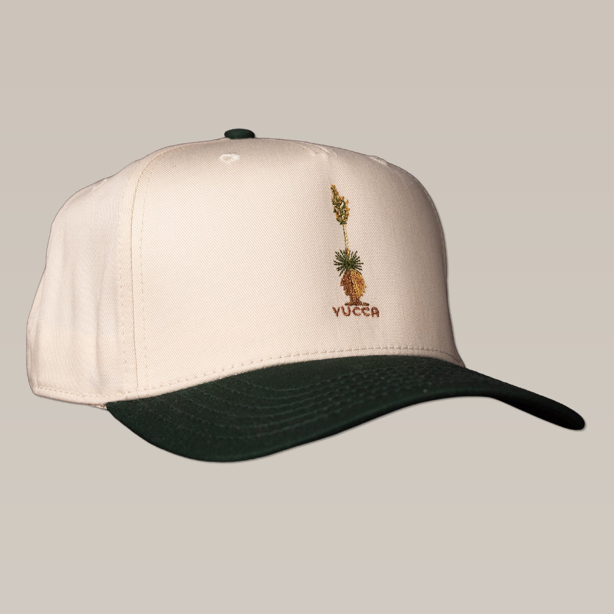 The Shop Hat | Yucca by Ballad of the Bird Dog is a beige baseball cap with a dark green brim, featuring an embroidered yucca plant and "YUCCA" on the front.
