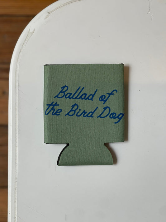 The Shop Koozie | Ballad of the Bird Dog by Ballad of the Bird Dog is a green can cooler featuring "Ballad of the Bird Dog" in blue script, displayed on a white surface.