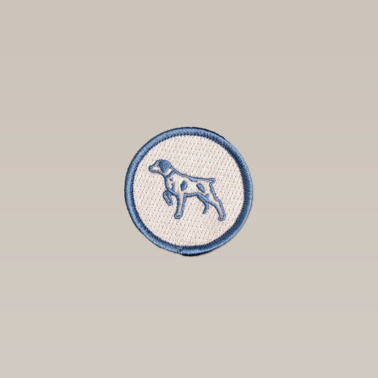 The Shop Patch | Ballad Merit Badge by Ballad of the Bird Dog features a circular, embroidered Bird Dog in profile on beige with a dark blue outline—perfect as a merit badge.
