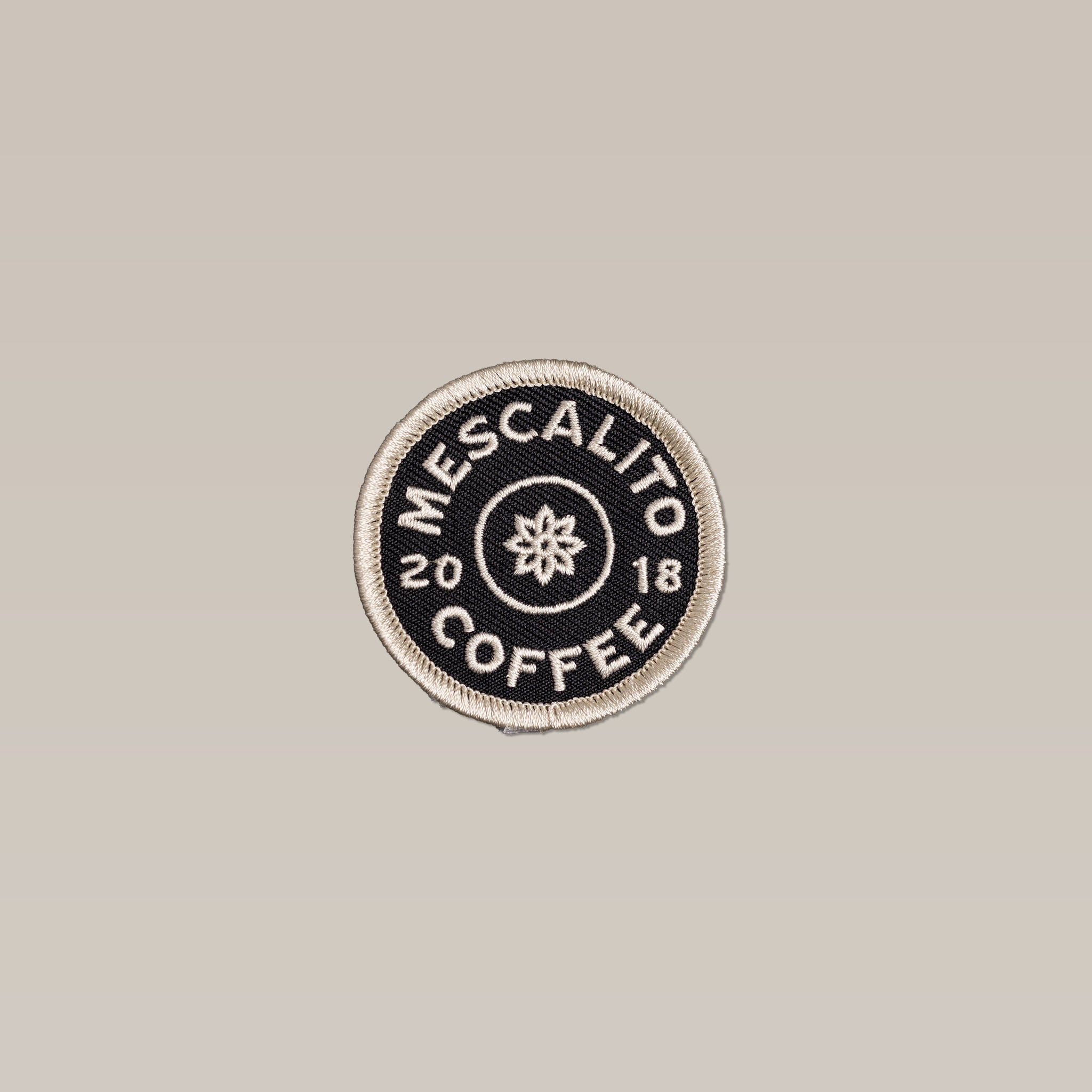 The Classic Circle Logo Patch by Mescalito Coffee is a handmade patch with "MESCALITO COFFEE 2018" in white on black and a simple flower at the center.