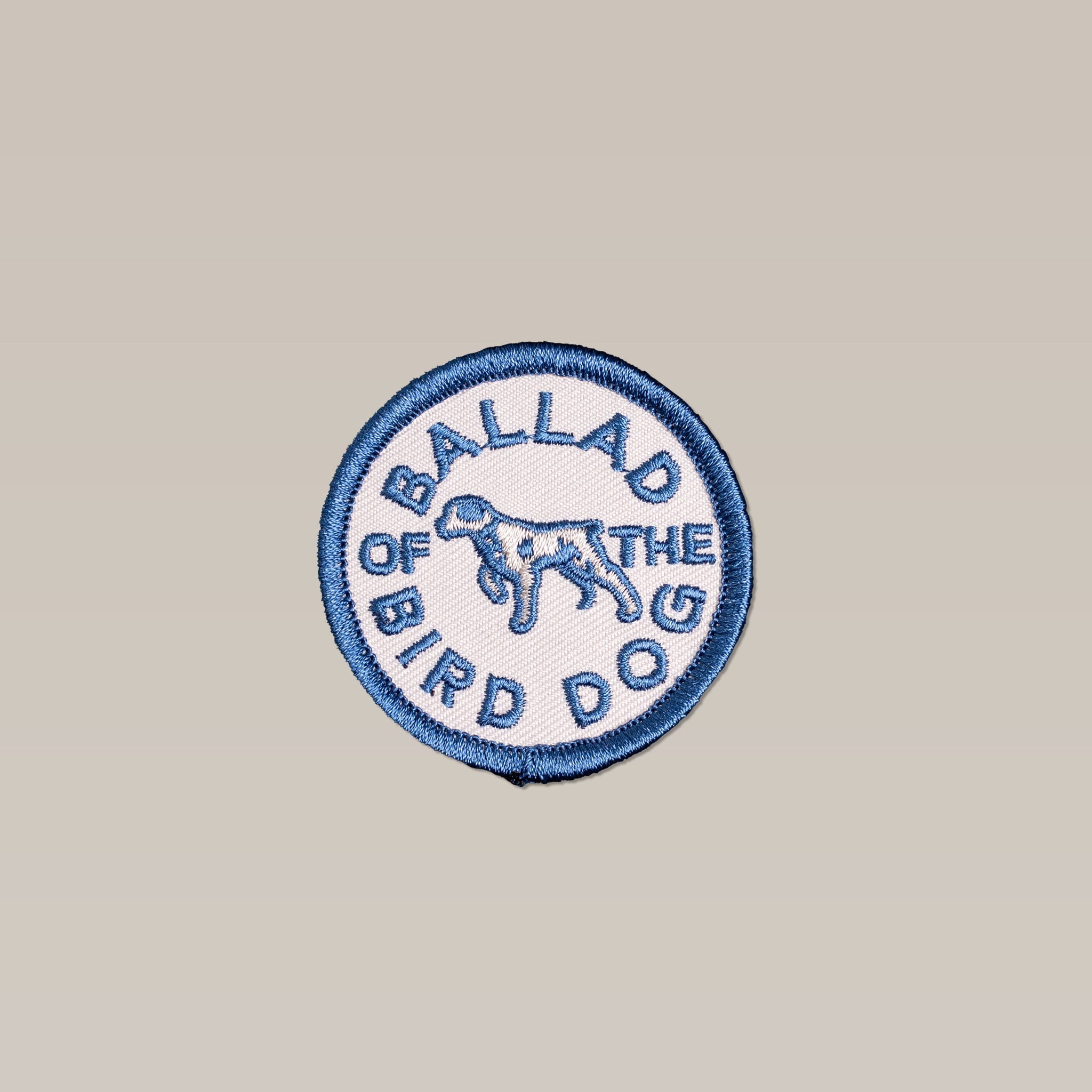 The Shop Patch | Clubhouse Tradition by Ballad of the Bird Dog features a round, light beige patch with a blue border and "BALLAD OF THE BIRD DOG" text encircling an outline of a standing dog.