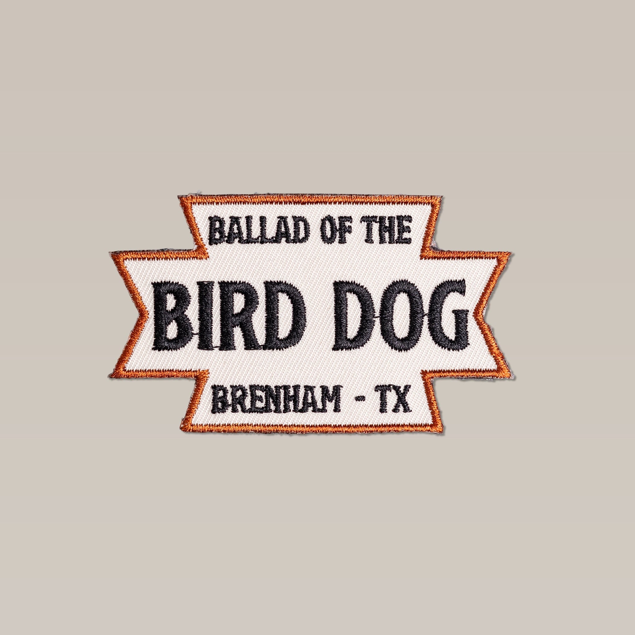 The Shop Patch | Desert Dog by Ballad of the Bird Dog is a rectangular embroidered patch with “Ballad of the Bird Dog, Brenham – TX” in black, an orange border, and a beige background.