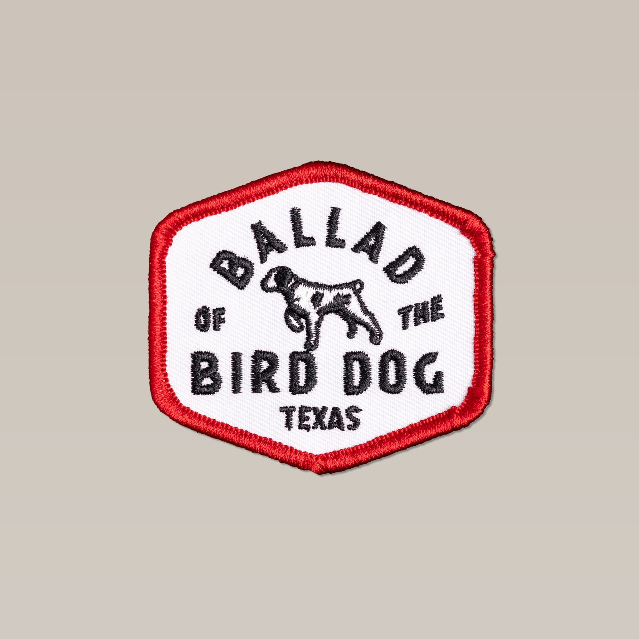 The Shop Patch | Field Companion by Ballad of the Bird Dog features a hexagonal design with a red border, black "Ballad of the Bird Dog Texas" text, and a dog outline—perfect for any patch collection.