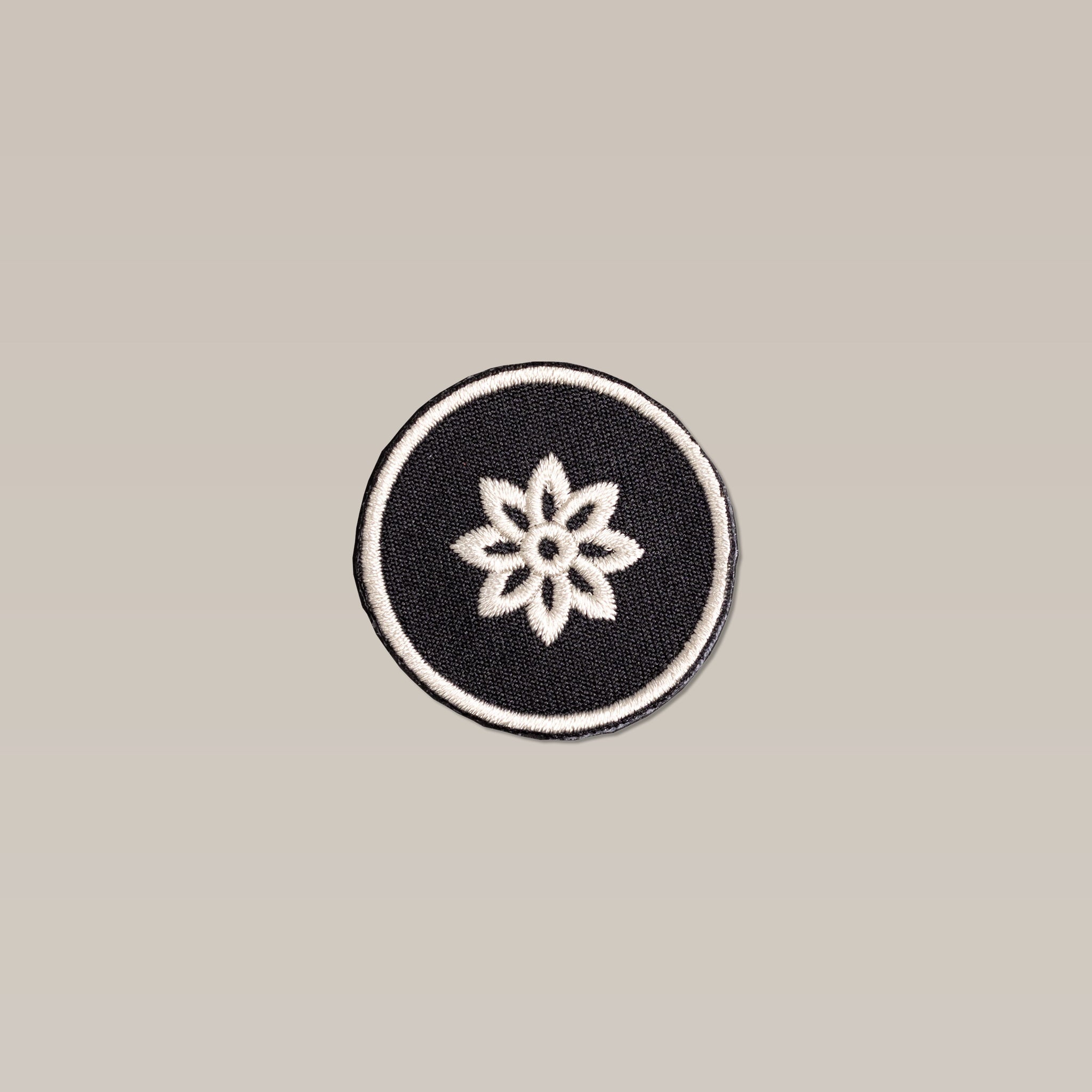 The Shop Patch | Flower Mescalito by Mescalito Coffee features a round black design with a central white eight-petal flower and white border, displayed on a plain beige background.