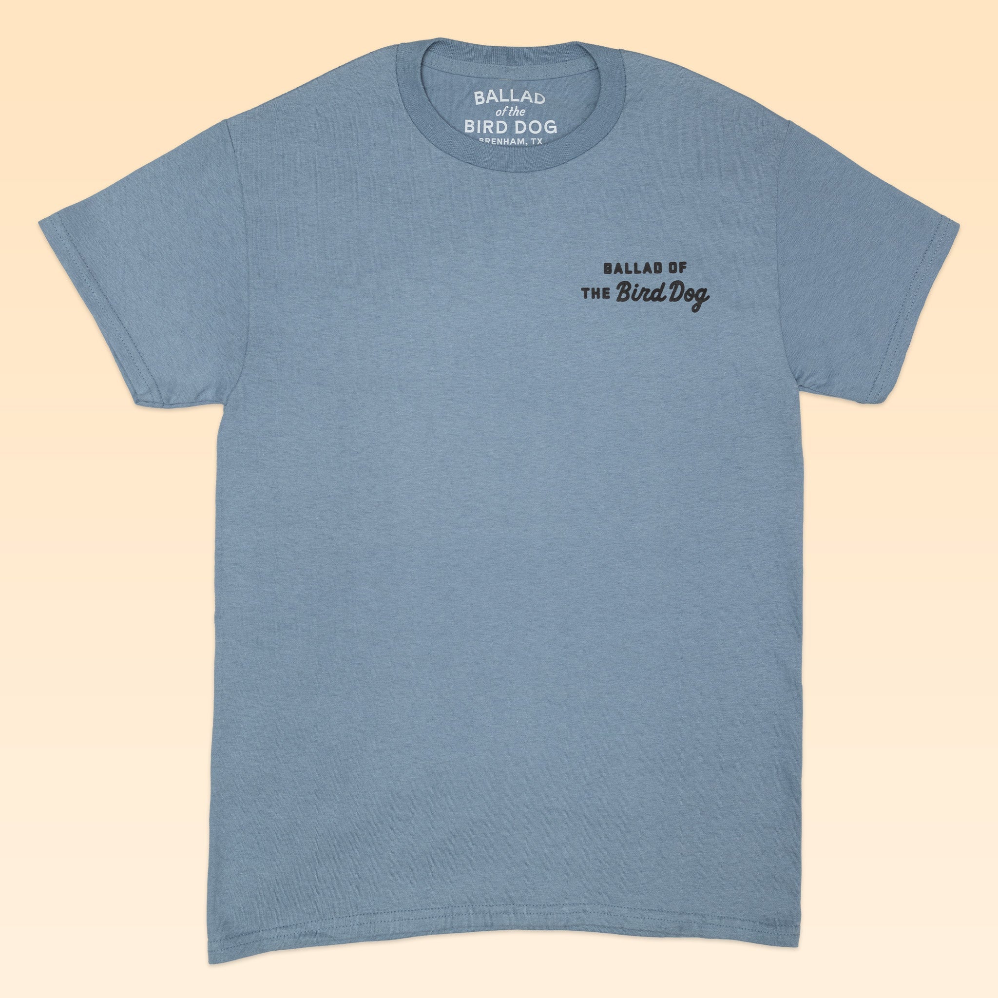 The Ballad of the Bird Dog "AZ to TX Journey" Shop Shirt is light blue, short-sleeve, with "BALLAD OF THE BIRD DOG" printed in black on the left chest and collar, laid flat on a beige background.