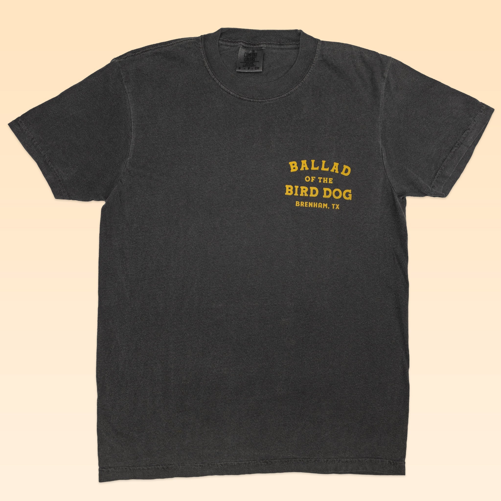 The Shop Shirt | Ballad Flag by Ballad of the Bird Dog is a vintage black tee with yellow "BALLAD OF THE BIRD DOG BRENHAM, TX" text on the left chest—ideal for fans of heritage style.