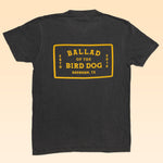 The Shop Shirt | Ballad Flag by Ballad of the Bird Dog is a vintage black tee with a yellow flag graphic on the back reading "Ballad of the Bird Dog, ESTD 2018, Brenham, TX," crafted on premium Comfort Colors Tees.