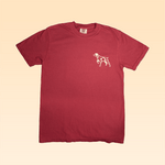 The Shop Shirt | Bird Dog Badge by Ballad of the Bird Dog is a plain red tee with a small white dog outline on the left chest, inspired by classic hunting shirts, shown on a beige gradient background.