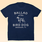 The Ballad of the Bird Dog Shop Shirt features a navy blue organic cotton tee with white "Ballad of the Bird Dog Brenham, TX" text and a bird dog illustration on the back—blending comfort and classic style.