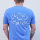 Show off your love for Ballad of the Bird Dog in the blue Shop Shirt featuring a Bird Dog Emblem and dog graphic on the back—perfect for a casual stroll through Downtown Brenham.