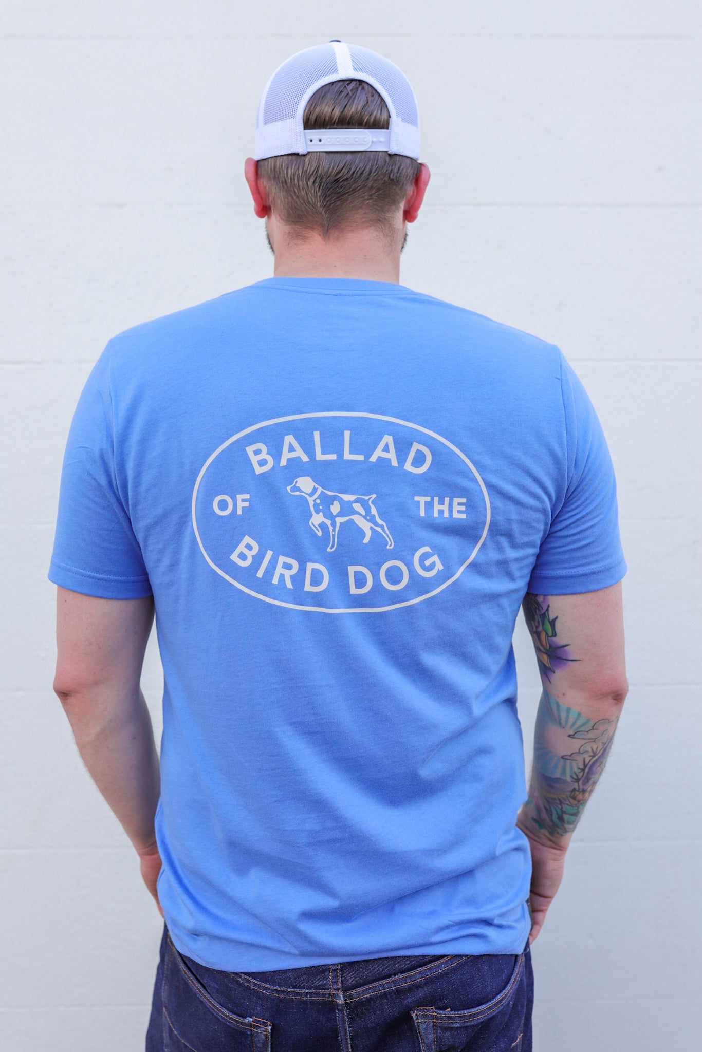 Show off your love for Ballad of the Bird Dog in the blue Shop Shirt featuring a Bird Dog Emblem and dog graphic on the back—perfect for a casual stroll through Downtown Brenham.