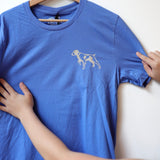 Someone holds the blue Shop Shirt | Bird Dog Emblem by Ballad of the Bird Dog, featuring a small dog outline on the upper left chest, proudly displaying their bird dog pride in Downtown Brenham.
