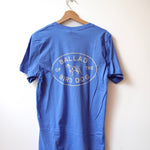 Show your bird dog pride with the Shop Shirt | Bird Dog Emblem by Ballad of the Bird Dog—a blue tee featuring an oval back graphic, bird dog illustration, and "Ballad of the Bird Dog" text, capturing downtown Brenham charm.