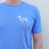 A person sporting the Ballad of the Bird Dog Shop Shirt featuring a light blue Bird Dog Emblem, perfect for displaying your bird dog pride in Downtown Brenham.