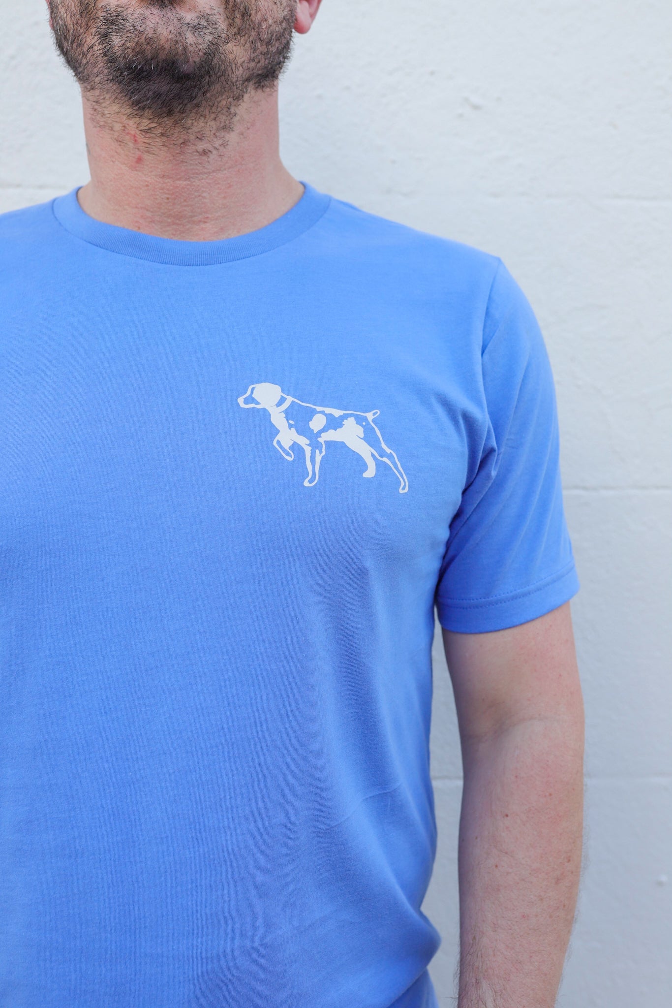 A person sporting the Ballad of the Bird Dog Shop Shirt featuring a light blue Bird Dog Emblem, perfect for displaying your bird dog pride in Downtown Brenham.