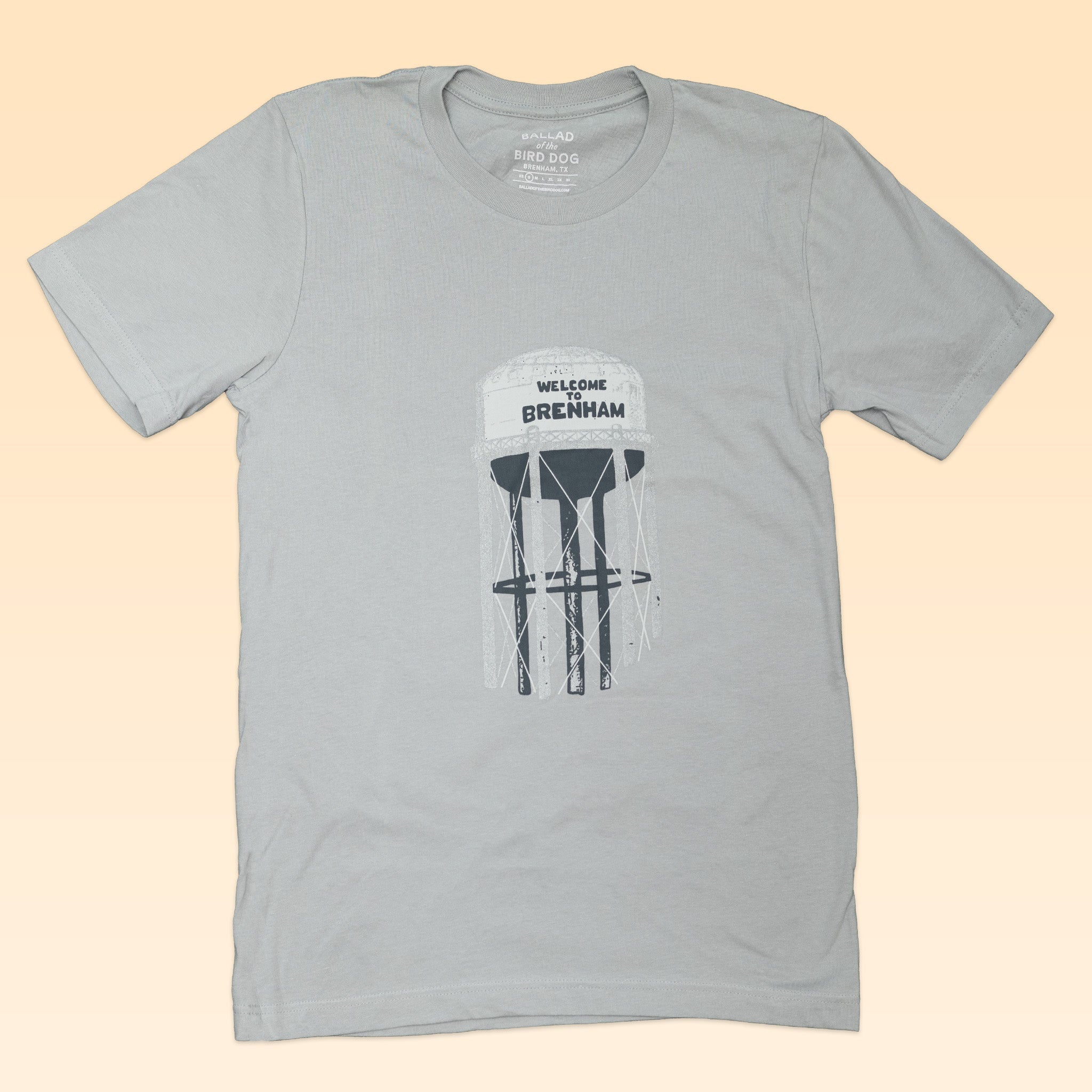 Show your Texas pride with the Ballad of the Bird Dog Shop Shirt, featuring a light gray Brenham Water Tank illustration and "Welcome Brenham" text—a must-have for locals.