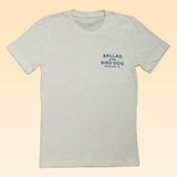 Shop the Ballad of the Bird Dog Circle Clubhouse Tradition Shop Shirt—a white tee with blue "BALLAD of the BIRD DOG BRENHAM, TX" text on the left chest, set against a pale peach background. Perfect for fans of this iconic style!.
