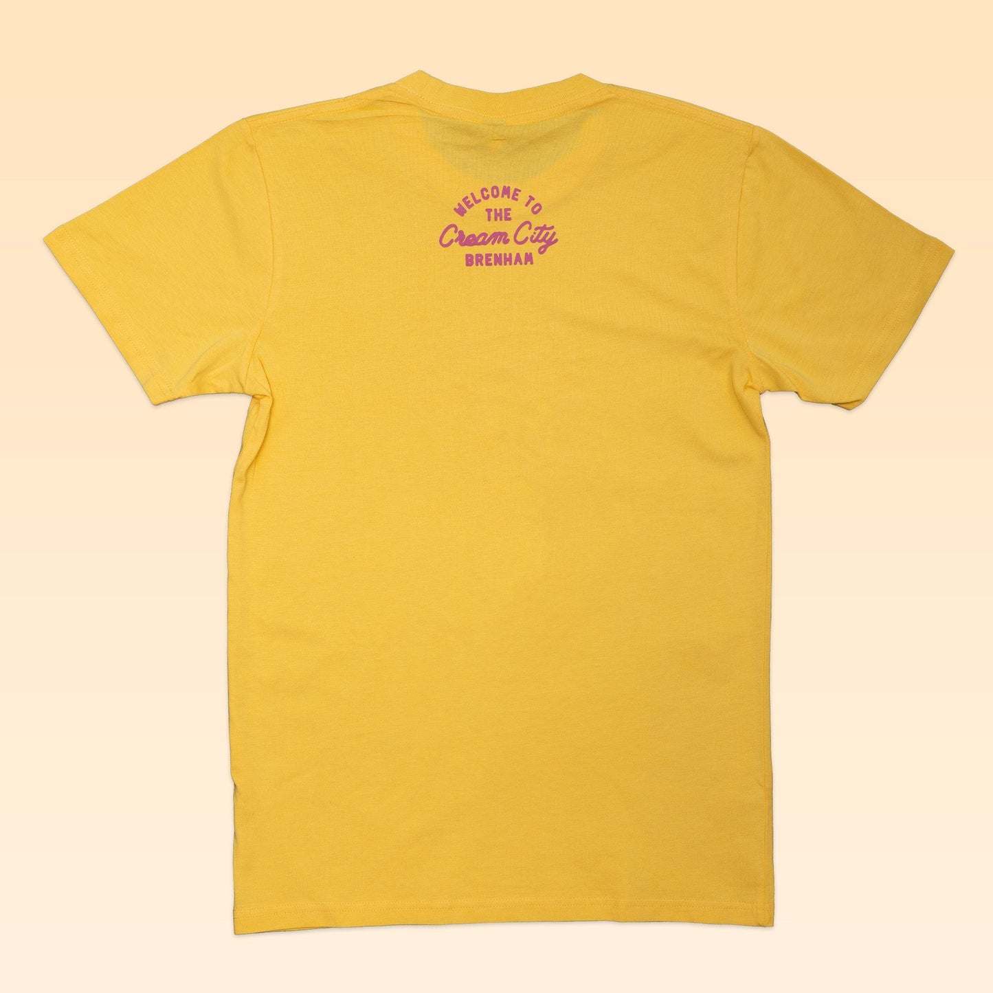 The Ballad of the Bird Dog Shop Shirt | Cream City is shown laid flat, back view, featuring purple "Welcome to the Cream City Brenham" text near the collar to honor Blue Bell Creameries' hometown.