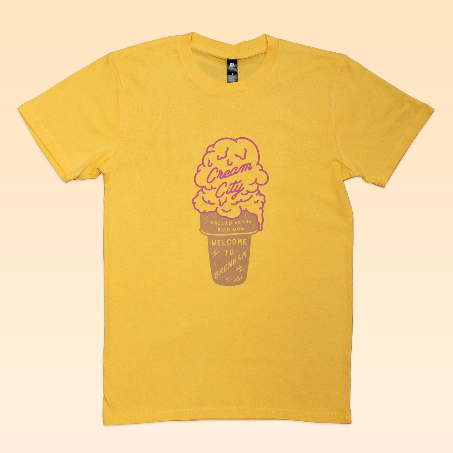 The Ballad of the Bird Dog Shop Shirt | Cream City features a yellow design with a pink ice cream cone and “Cream City” text—celebrating Brenham, hometown of Blue Bell Creameries.