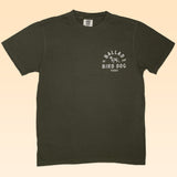 The Shop Shirt | Desert Covey Flush by Ballad of the Bird Dog is an olive green, hand-printed outdoor tee featuring a small white "Ballad of the Bird Dog Texas" graphic with a dog illustration on the left chest.
