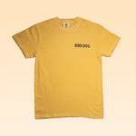 The Shop Shirt | Desert Dog by Ballad of the Bird Dog is a plain yellow adventure shirt featuring "BIRD DOG" in black on the left chest, shown against a light beige background.