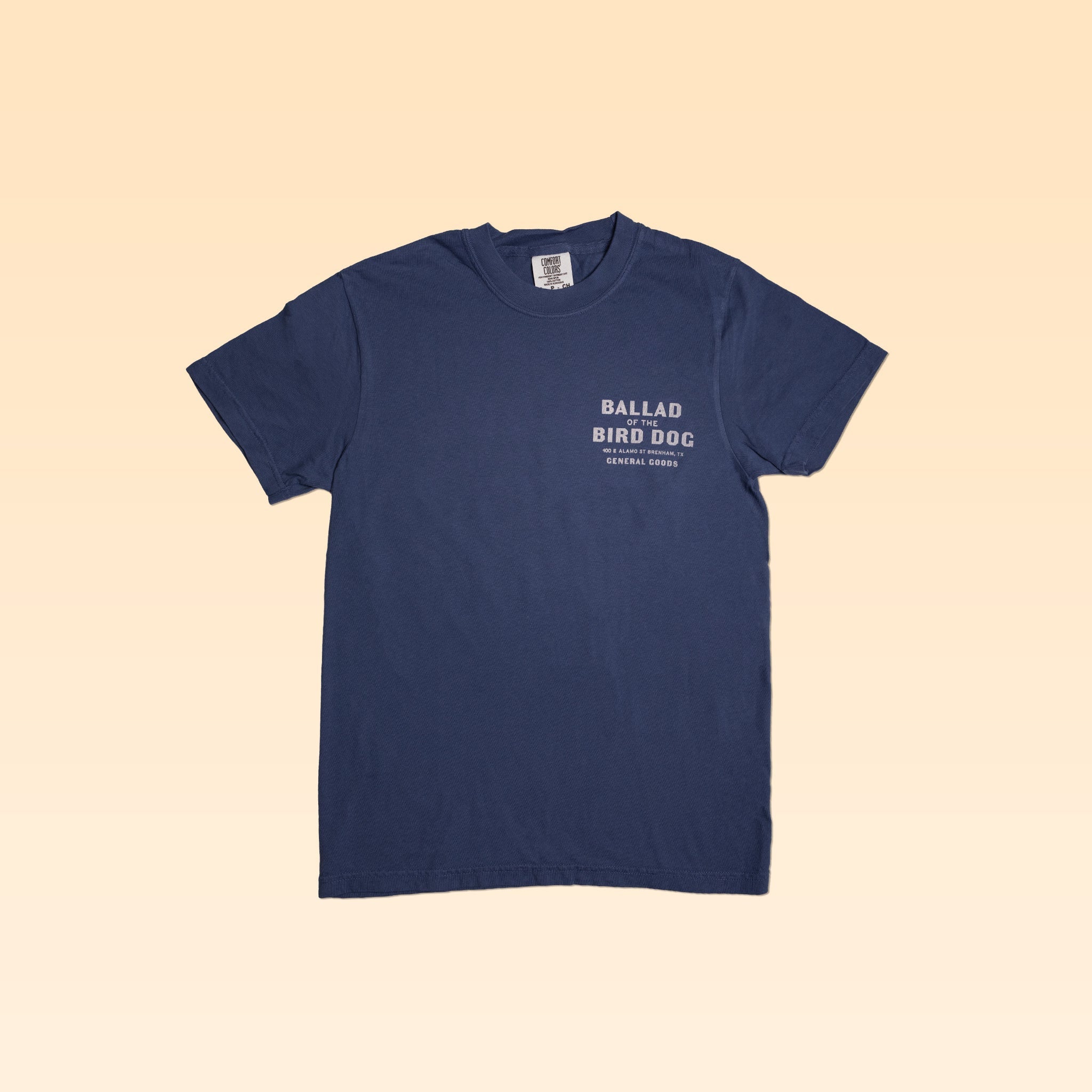 The Shop Shirt | General Goods by Ballad of the Bird Dog is a navy blue tee with "BALLAD BIRD DOG GENERAL GOODS" in white on the left chest, inspired by classic general goods stores, shown on a light beige background.
