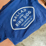 The Shop Shirt | Home Base by Ballad of the Bird Dog is a blue Comfort Colors tee featuring white text: "Ballad of the Bird Dog, 100 E Alamo St, Brenham, TX," displayed on a brown surface.