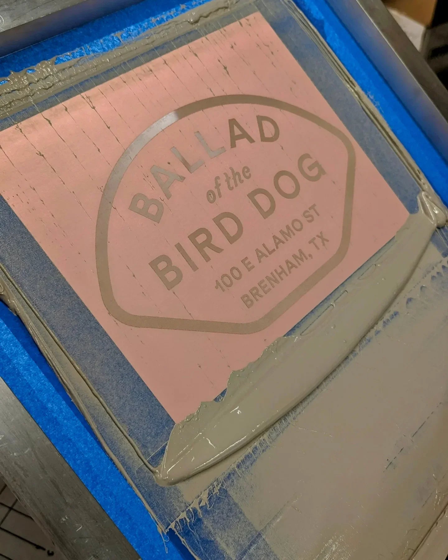 A screen printing frame with a "BALLAD of the BIRD DOG, 100 E ALAMO ST, BRENHAM, TX" stencil and gray ink, made for the Shop Shirt | Home Base by Ballad of the Bird Dog.