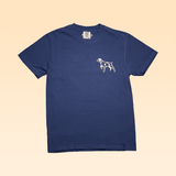 The Shop Shirt | Home Base by Ballad of the Bird Dog is a navy Comfort Colors tee, featuring a small white dog graphic on the left chest and shown on a beige background.