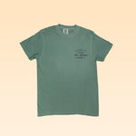 A sage green Shop Shirt by Ballad of the Bird Dog with short sleeves features black text, "Hills of the mid 800s, La Salina, Helum, TX," on the left chest. Product name: La Lobina.